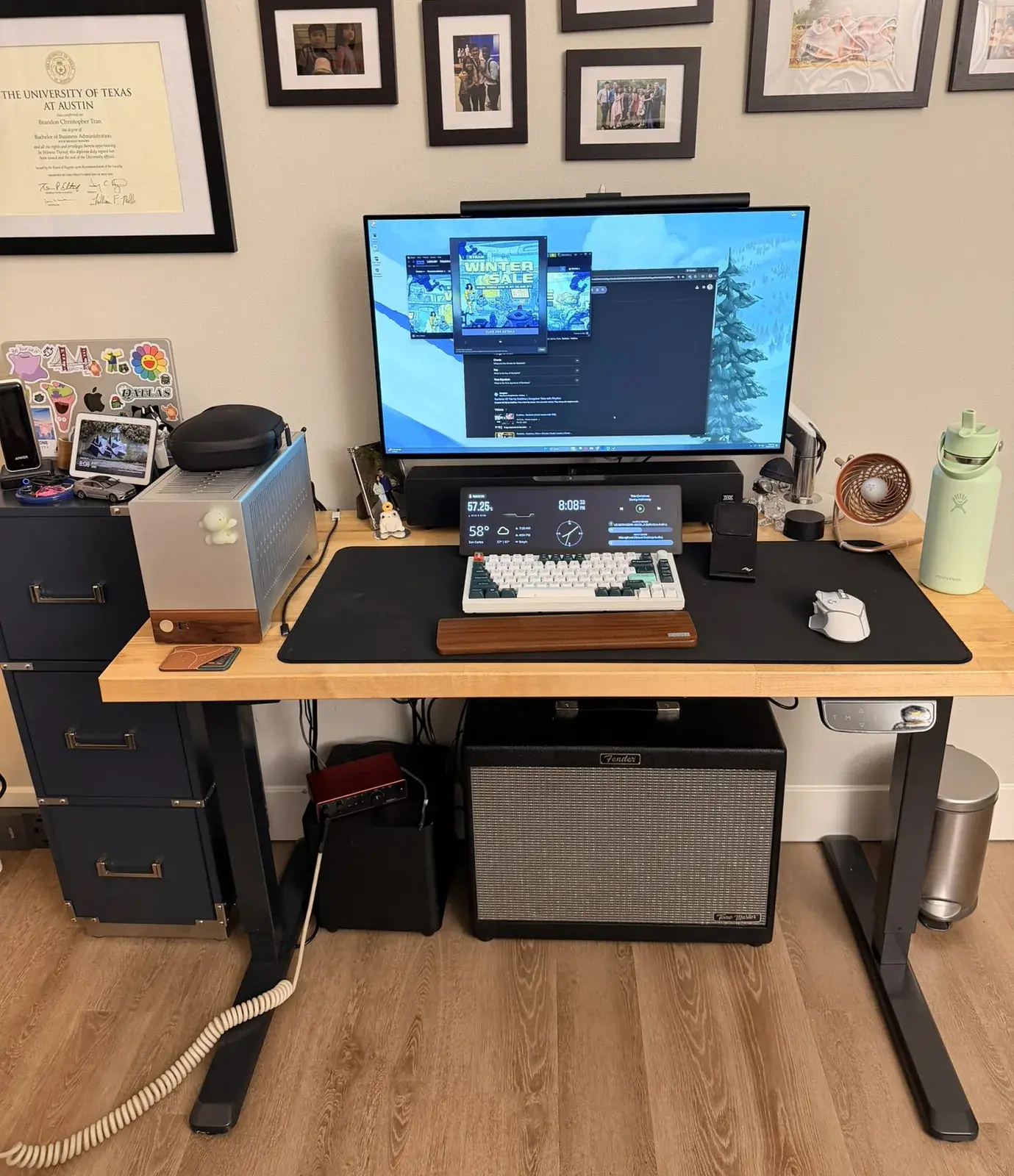 My whole desk: the butcher block top on its black legs, the monitor and its light bar, the Terra on the left, my Fender under it, our photos on the wall above.