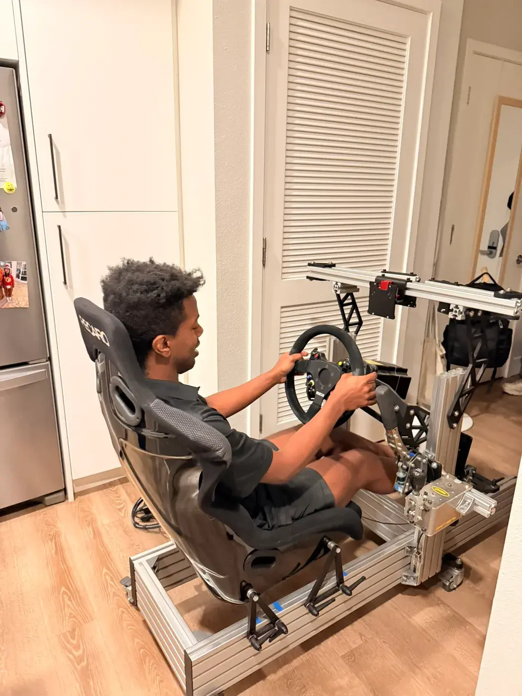 A friend trying the first version: the Recaro seat, wheel and pedals on the bare chassis, no screens yet.