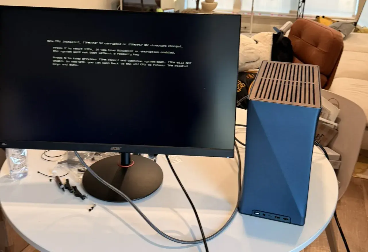 The sim's PC at its first boot: the blue Fractal Era 2 on a round white table, spare screws beside the monitor, the screen still on its BIOS message about the new CPU.